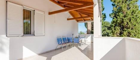 A covered outdoor area with a wooden ceiling, a white wall with a window, and a row of blue chairs.
