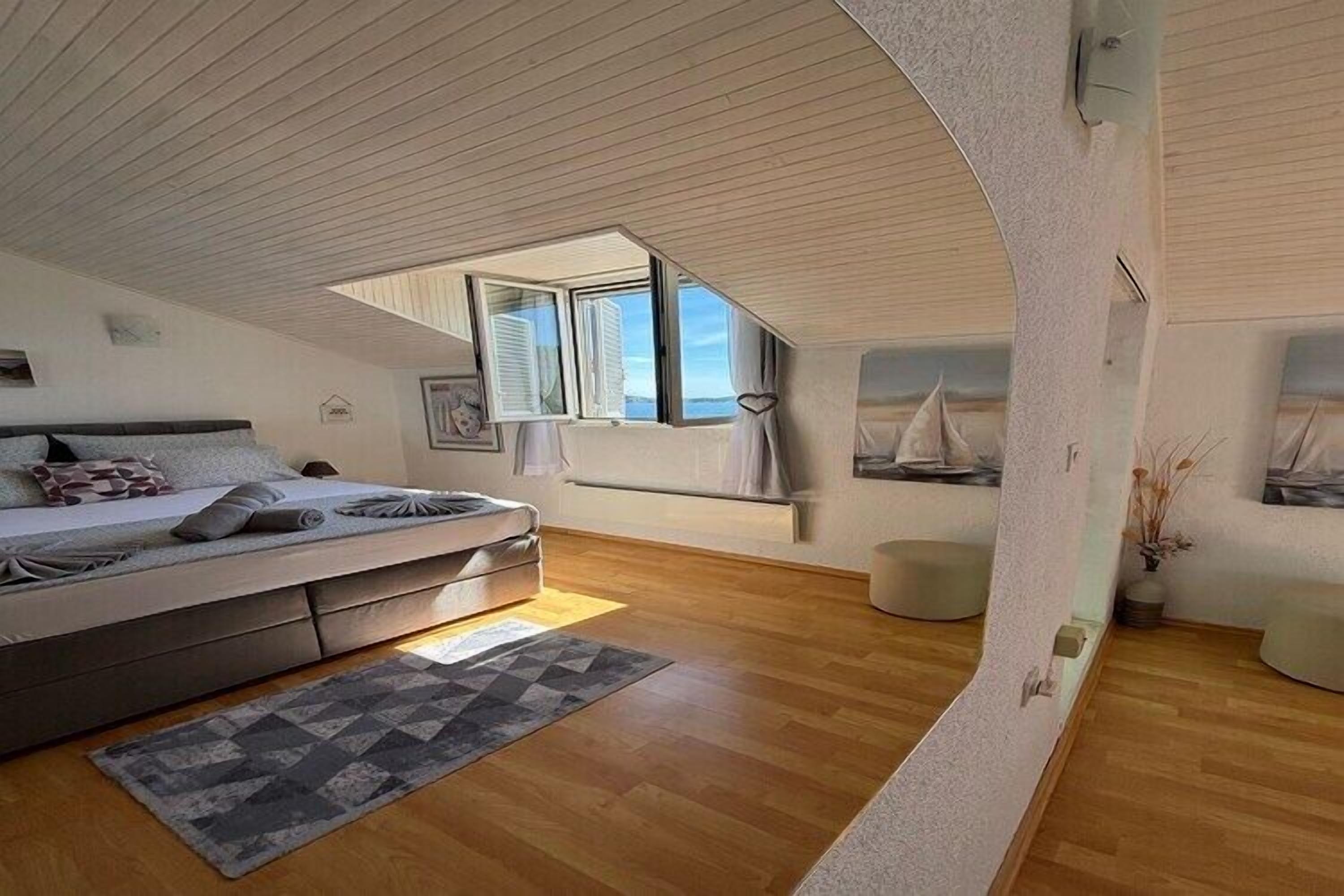 A bedroom with a loft-style ceiling, a bed, a window, and a view of the sky.
