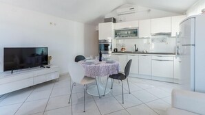 A modern kitchen with white cabinets, a dining table with chairs, and a flat-screen TV on a white console.