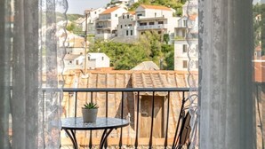 A balcony with a small round table and a potted plant, overlooking a hillside with terraced houses.