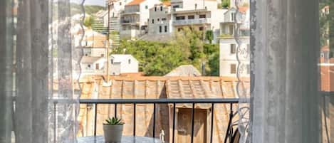A balcony with a small round table and a potted plant, overlooking a hillside with terraced houses.
