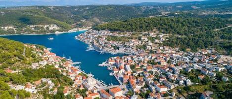 An aerial view of a coastal town with a marina, surrounded by hills and a clear blue sea.