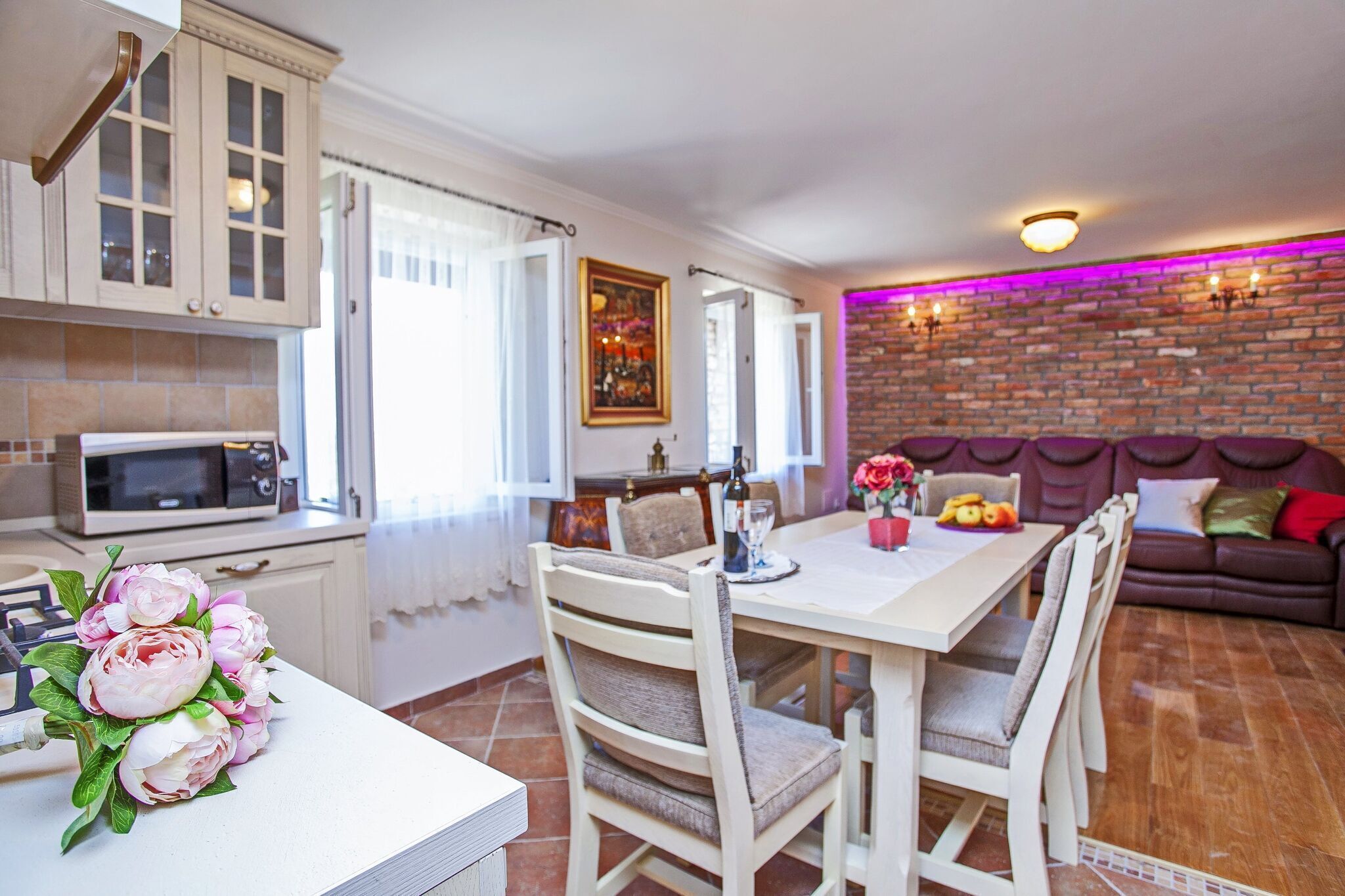 A dining area with a white table and chairs, a bouquet of flowers, and a brick wall with a neon light.