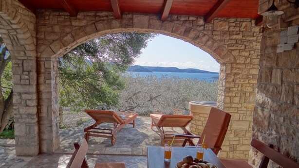 A stone archway leading to a terrace with wooden furniture and a table set for two, overlooking a scenic landscape.
