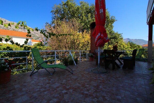 Relax in style on this patio, complete with a lounge chair, dining table, and umbrella, surrounded by lush greenery and breathtaking mountain views.