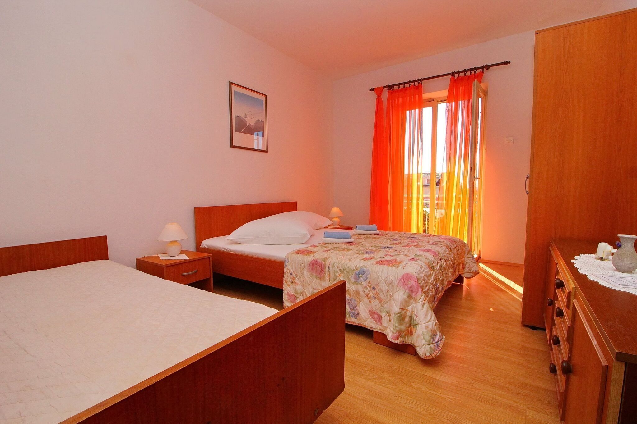 A bedroom with two beds, a wooden wardrobe, and a bedside table with a lamp.