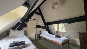 Une chambre mansardée accueillante, avec deux lits, un petit tabouret et une armoire en bois.