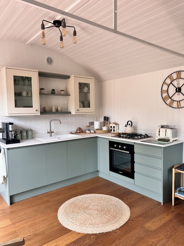 A kitchen with light blue cabinets, a white countertop, a round woven rug, and a modern light fixture. - Sunset - nestled in a wildflower meadow on a farm with Highland Cows (PULBOROUGH)