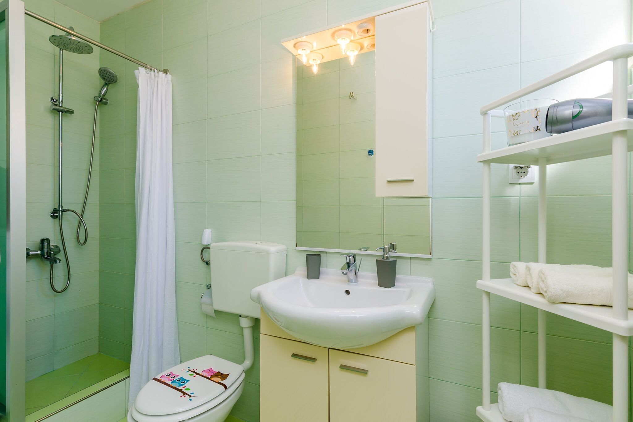Ein Badezimmer mit Dusche, Toilette, Waschbecken und einem Ablagefach mit Handtüchern.