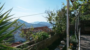 Un jardín con un muro de piedra, una pérgola y vistas a casas y montañas.