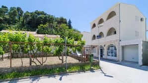 Um edifício com fachada branca e janelas em arco, um jardim cercado com videiras e um céu claro.