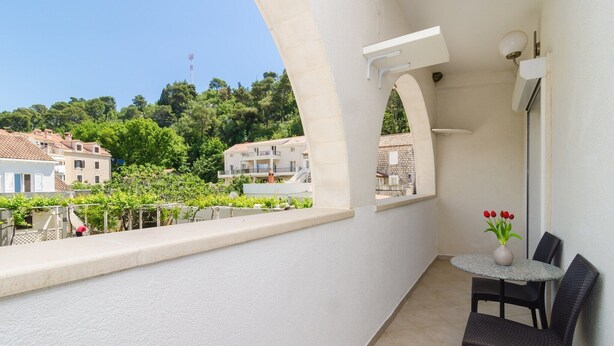 Varanda com mesa redonda e cadeiras, vaso com flores e vista para edifícios e vegetação.