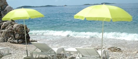 A beach with white lounge chairs and yellow umbrellas.