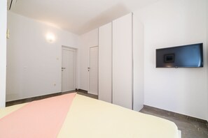 Una habitación con una cama, un televisor instalado en la pared y una puerta.