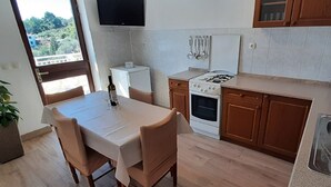 Eine kleine Küche mit Esstisch, Stühlen, Herd, Kühlschrank und einem an der Wand befestigten Fernseher.