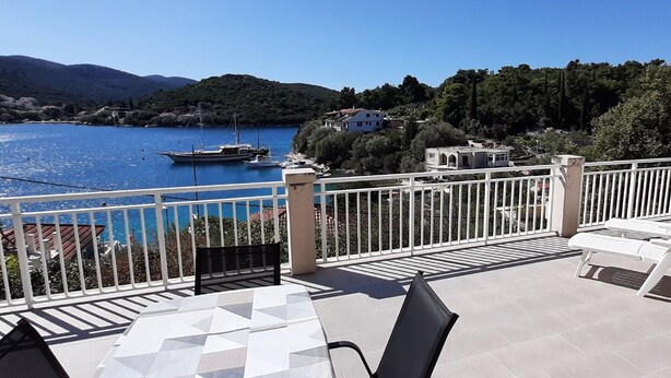 Eine Terrasse mit Blick auf eine Bucht, Boote und eine gebirgige Landschaft.