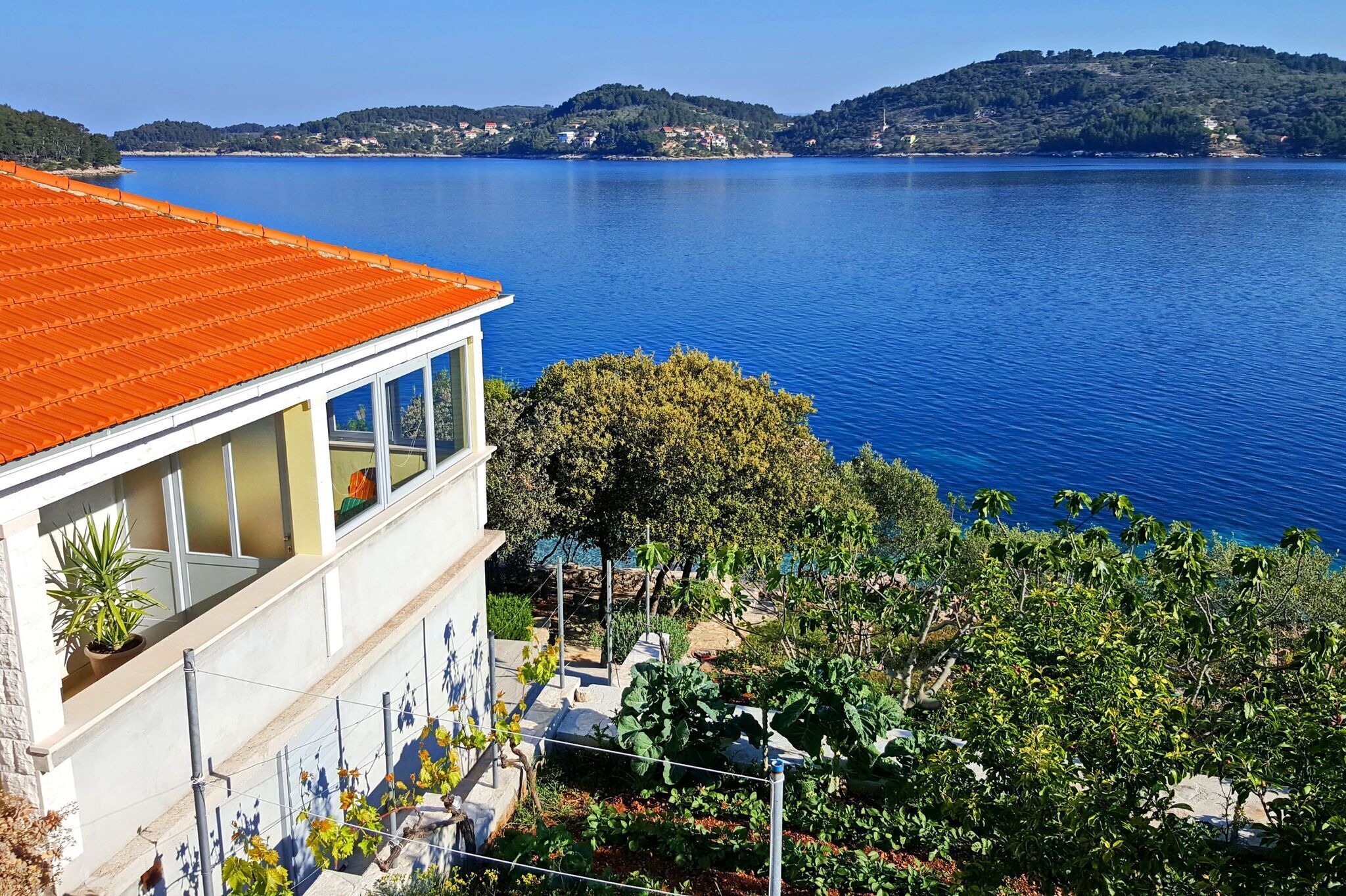A building with a red roof overlooking a calm lake, surrounded by greenery and hills in the background.