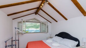 A bedroom with a bed, a nightstand, a lamp, a window with a view of the sea, and a wooden ceiling.