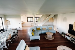 A spacious living area with a light blue sectional sofa, a dining table with chairs, a staircase, and a television on a stand. - Country House 'Camino Blanco' with Private Pool, Shared Terrace and Air Conditioning (IBEAS DE JUARROS)