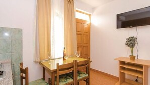 Un coin repas avec une table et des chaises en bois, un téléviseur fixé au mur et une petite plante posée sur une table d’appoint.