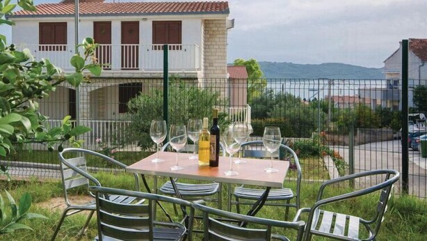 Un espace extérieur aménagé pour prendre les repas, avec une table et des chaises, une bouteille de vin et une vue sur un bâtiment dont le toit est recouvert de tuiles rouges.