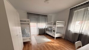Ein Schlafzimmer mit Etagenbetten, einem Kleiderschrank, einem Schreibtisch mit Stuhl und einem fenster mit Vorhängen.
