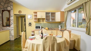 Un coin repas avec une table dressée pour quatre personnes, une cuisine équipée d’un four à micro-ondes et une fenêtre avec des rideaux.