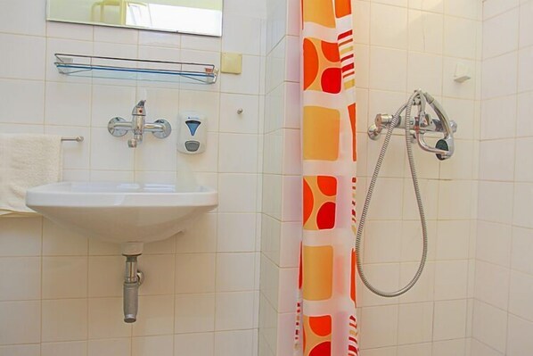 A bathroom with a white sink, a mirror, a shower with a colorful curtain, and a towel rack. - Apartment&Rooms Savonari - Two Bedroom  Studio Apartment with Terrace (Orasac)