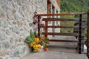 A stone wall with a wooden gate, a potted plant with yellow flowers, and a staircase leading to a wooden deck.