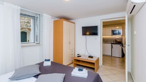 Habitación de hotel con cama, televisión, escritorio y una kitchenette al fondo.