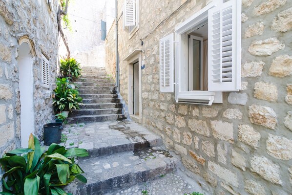 Eine schmale Steintreppe führt zu einem Gebäude mit weißen Fensterläden und einem kleinen Fenster.