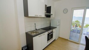 Una cocina compacta con gabinetes blancos, un lavamanos de acero inoxidable y un horno empotrado.