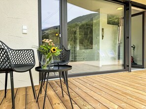 A modern outdoor seating area with two chairs and a small table, a vase with flowers, and a glass door leading to a deck with a view of a mountain. - Lovely apartment for 4 people with WIFI, TV and terrace (Urgen)