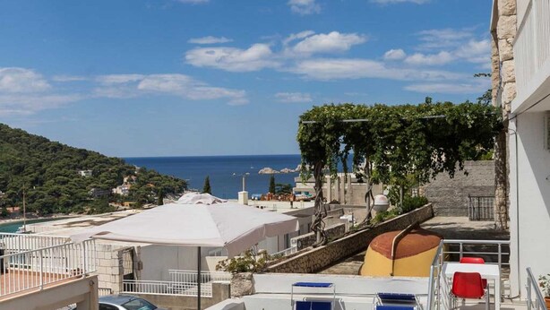 A coastal building with a view of the sea, a rooftop terrace with umbrellas, and a stone wall. - One Bedroom apartment with terrace (Dubrovnik)