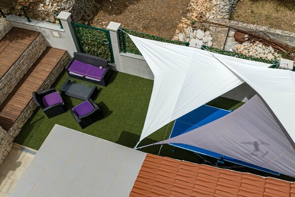 A patio area with a seating arrangement, a white shade sail, and a stone wall.