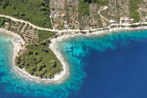 An aerial view of a coastal area with a small island, clear turquoise waters, and a densely vegetated shoreline.