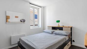 Un dormitorio con cama, mesita de noche, lámpara y ventana.