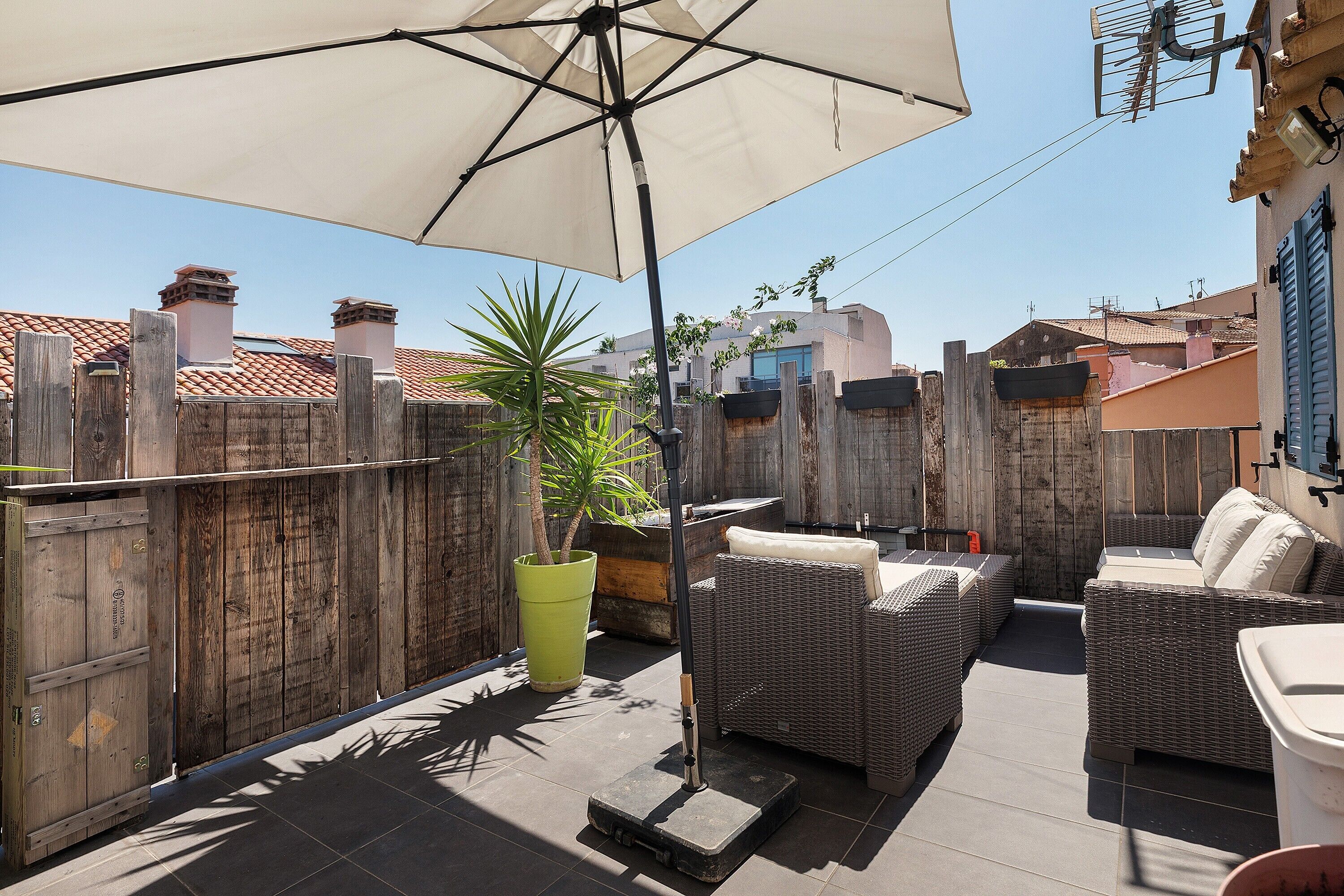Une terrasse extérieure aménagée avec des meubles en osier, un grand parasol et une clôture en bois.