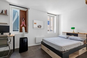 Une chambre à coucher moderne avec un lit, des tables de chevet, un bureau avec un ordinateur et une fenêtre.