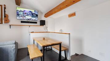 Une petite pièce avec une table et un banc en bois, un téléviseur fixé au mur et une guitare appuyée contre le mur.