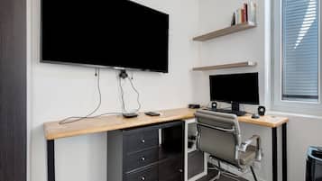A modern office space with a large flat-screen monitor, a desk with a computer, a chair, and a window with blinds.