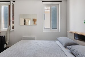 A bedroom with a bed, a nightstand, a mirror, and two windows. - Apartment 'Appartement Terrasse Sur Le Port' with Private Terrace, Balcony and Wi-Fi (La Seyne-sur-Mer)