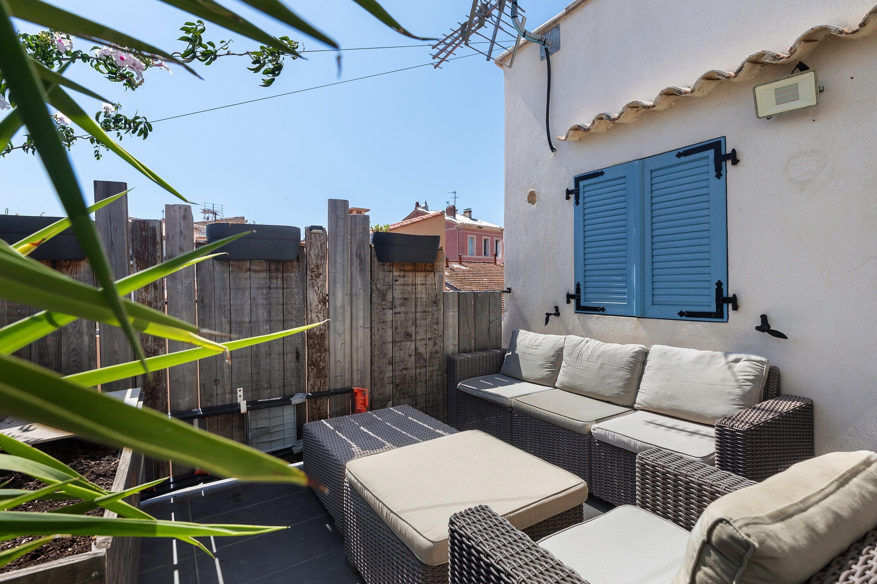 Un espace extérieur aménagé avec des meubles en osier et une fenêtre à volets bleus.
