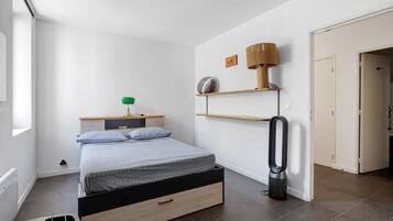 A bedroom with a bed, bedside table, lamp, and a vacuum cleaner.