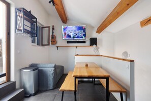 Un espace de vie compact comprenant un banc en bois, un téléviseur fixé au mur, une guitare et une petite table.