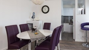 A modern dining area with a round table, purple upholstered chairs, a decorative clock, and a pendant light.