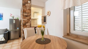 Une cuisine moderne avec un mur d’accent en pierre, un coin repas doté d’une table ronde en bois et une fenêtre avec des stores.