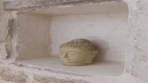A stone Buddha statue in a niche within a stone wall.