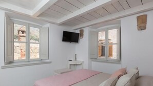 Un dormitorio con una cama, un televisor y dos ventanas.