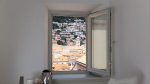 Una habitación con ventana que da a un pueblo en la ladera, de casas muy juntas.